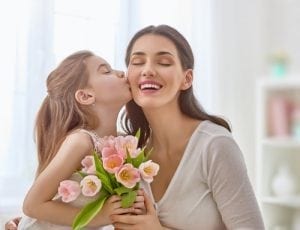Child daughter congratulates mom and gives her flowers tulips
