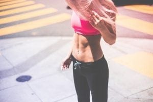 Fit woman with pink hair looking down at her abs