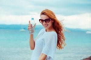 Beautiful young brunette woman in sunglasses drinking water and cooling off after running at the beach on a sea 