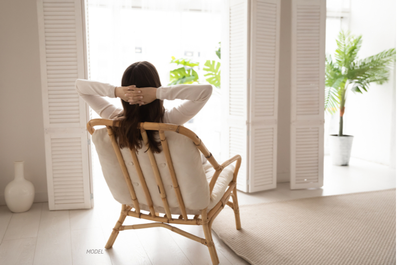 Woman resting in a chair, looking outside with her hands behind her head.